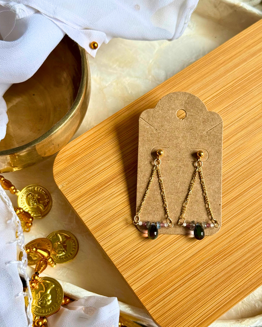 Gold earrings on a wooden display card with coins and a white cloth in the background.
