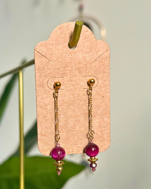 Gold chain earrings with pink beads on a cardstock earring card against a blurred natural background