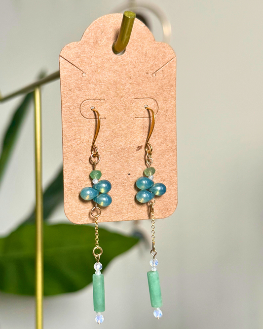 Pair of earrings with green and blue beads on a cardstock earring card against a blurred natural background