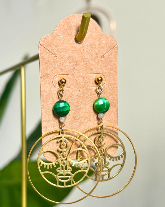Gold earrings with green beads on a cardstock earring card against a blurred natural background