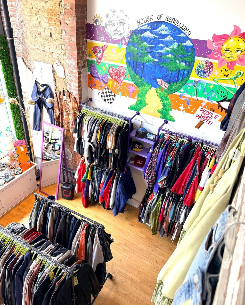 Second-hand clothing store with racks of clothes and a colorful mural on the wall.