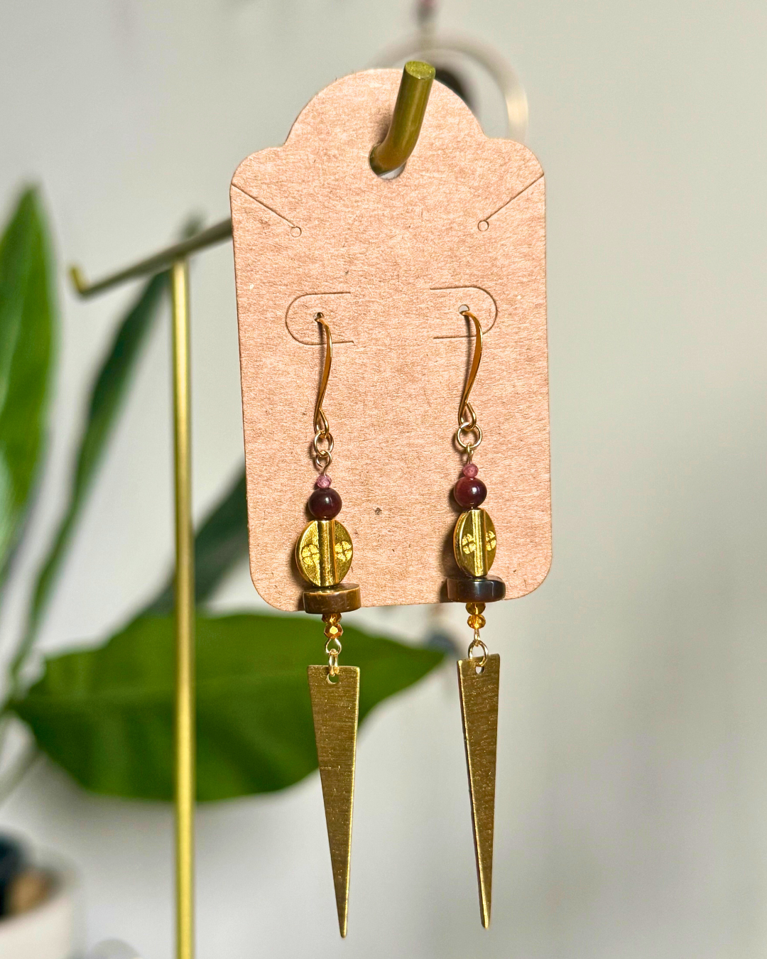 Pair of gold earrings with beads on a cardstock earring card against a blurred natural background