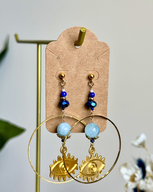 Gold hoop earrings with blue beads on a beige card against a light background